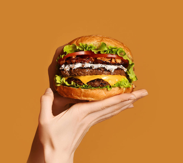 Woman hands hold big double cheeseburger burger sandwich with beef and bacon on yellow - Фото, зображення
