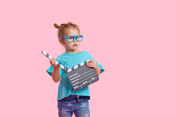 Funny smiling child girl in cinema glasses hold film making clapperboard isolated on pink background. Studio portrait. Childhood lifestyle concept. Copy space for tex - Foto, Imagen