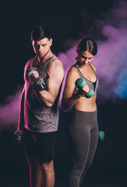Sporty young couple with dumbbells on dark background - Фото, зображення
