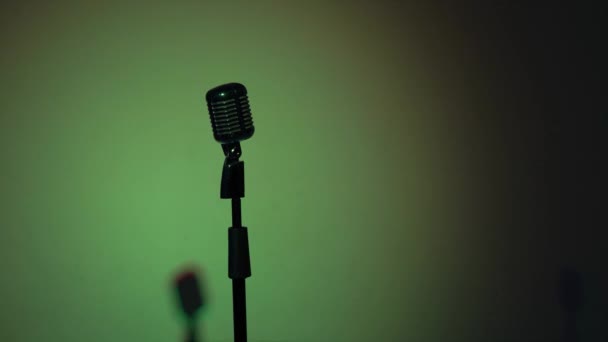 Professionele concert vintage microfoon voor opnemen of spreken met publiek op stand in donkere lege retro club. De schittering van de blauwe schijnwerpers knippert elke seconde op een chromen microfoon op groene achtergrond. - Video
