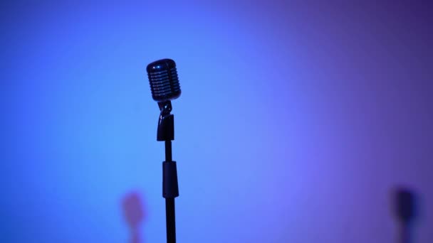 Профессиональный концертный винтажный серебряный микрофон для записи или выступления перед аудиторией на сцене в темном пустом ретро-клубе крупным планом. Spotlights светятся на хромированном микрофоне на многоцветном фоне
. - Кадры, видео