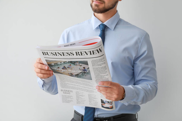 Handsome businessman with newspaper on light background - Photo, Image