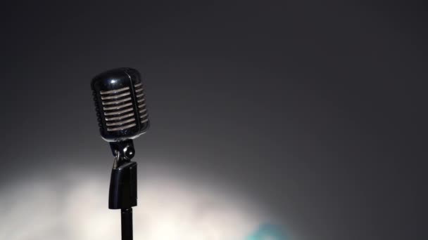 Professzionális koncert vintage glare mikrofon rekord vagy beszélni közönség a színpadon sötét üres retro klub közeli. Spotlights ragyog egy króm mikrofon a bal oldalon szürke háttér. - Felvétel, videó
