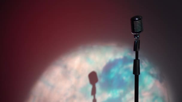 Professionele concert vintage glare microfoon voor opnemen of spreken met publiek op het podium in donkere lege retro club close-up. Spotlights schijnen op een chroom microfoon aan de rechterkant op multi color achtergrond. - Video