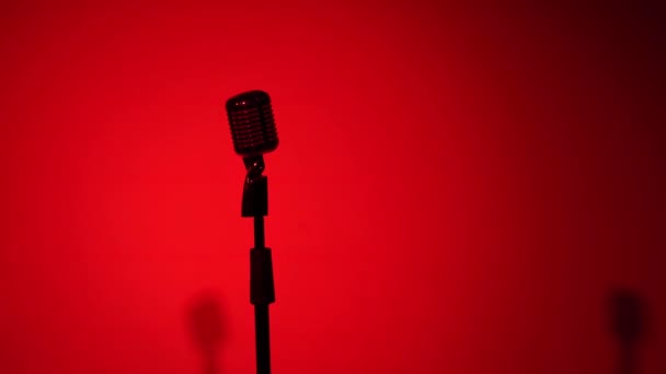 Professionele concert vintage glare microfoon voor opnemen of spreken met publiek op het podium in donkere lege retro club. Licht van schijnwerpers verandert en glans op chroom mic op rode en blauwe achtergrond. - Video