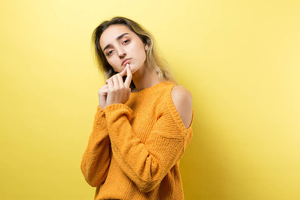 Portrait of a beautiful girl in an orange sweater, looks aside with pensive expression, is considering a plan for further action. - Foto, immagini