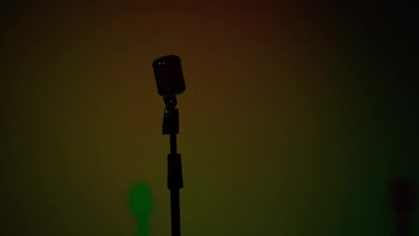 Professionelle Konzert Vintage Blendung Mikrofon für Platte oder sprechen Sie mit dem Publikum auf der Bühne in dunklen leeren Retro-Club in Großaufnahme. Scheinwerfer leuchten auf einer Silhouette aus Chrommikrofon auf mehrfarbigem Hintergrund. - Filmmaterial, Video