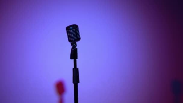 Professionele concert vintage glare microfoon voor opnemen of spreken met publiek op het podium in donkere lege retro club close-up. Spotlights veranderen en schijnen op een chroom microfoon op rode en blauwe kleur achtergrond. - Video