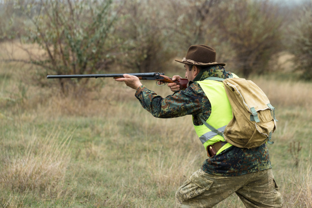Un cazador con un arma en sus manos y un perro de caza en un chaleco naranja reflectante caza a un faisán en la estepa
. - Foto, Imagen