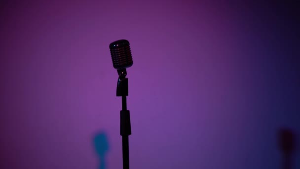 Silhouette of concert vintage glare mikrofon felvételre, vagy beszéljen a közönséggel a színpadon sötét üres retro klub közeli. A kék reflektorfény bekapcsolja és megvilágítja a króm mikrofont fehér alapon. - Felvétel, videó