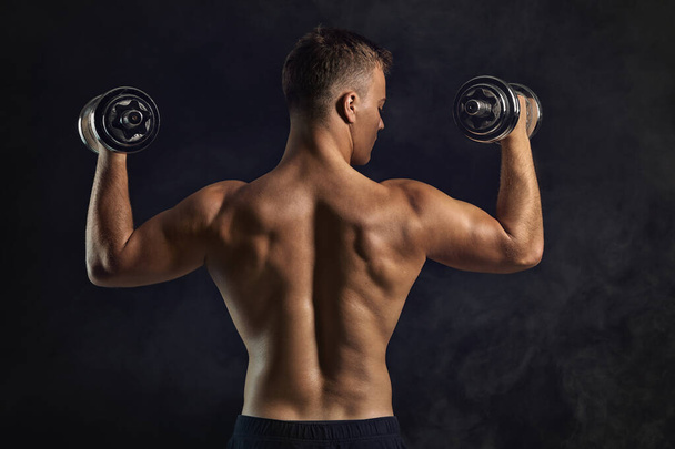 Jóképű férfi testépítő súlyzókkal sötét háttéren - Fotó, kép
