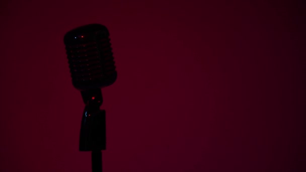 Silhouette von professionellen Konzert Vintage Blendung Mikrofon für Platte oder sprechen mit dem Publikum auf der Bühne in leeren Retro-Club in Großaufnahme. Roter Scheinwerfer leuchtet schwach auf einem Chrommikrofon auf dem dunklen Hintergrund. - Filmmaterial, Video