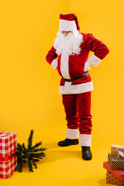 Noel Baba ellerini kemere koyuyor ve yerdeki hediyelere bakıyor. - Fotoğraf, Görsel