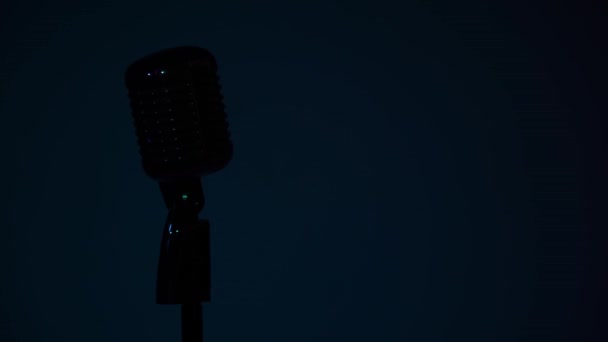 Professional concert vintage glare microphone for record or speak to audience on stage on a dark blue background in empty retro club close up. Red spotlight blink on silhouette of a chrome mic one second. - Footage, Video