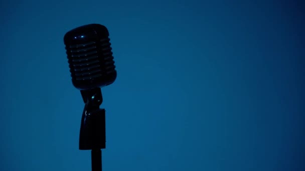 Le projecteur bleu s'allume et éclaire le micro chromé sur fond sombre. Concert professionnel vintage microphone éblouissant pour enregistrement ou parler au public sur scène dans un club rétro vide gros plan
. - Séquence, vidéo