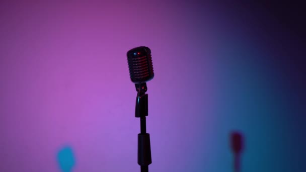 Professionelle Konzert Vintage Blendung Mikrofon für Platte oder sprechen Sie mit dem Publikum auf der Bühne in dunklen leeren Retro-Club in Großaufnahme. Scheinwerfer leuchten auf einem Chrommikrofon in der Mitte auf mehrfarbigem Hintergrund. - Filmmaterial, Video