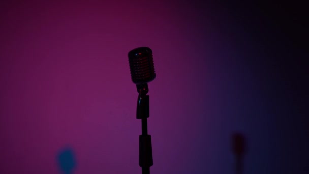 Professional vintage glare microphone for record or speak to audience on stage in dark empty retro club close up. Spotlights turn on and shine on a chrome mic on the right on multi color background. - Footage, Video