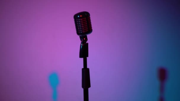 Professional vintage glare microphone for record or speak on stage in dark empty retro club close up. Spotlights shine on a chrome mic in middle on multi color background. The camera moves away. - Footage, Video