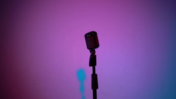 Microphone professionnel vintage éblouissant pour enregistrer ou parler sur scène dans un club rétro sombre vide de près. Les projecteurs brillent sur un micro chromé au milieu sur fond multicolore. La caméra approche.
. - Séquence, vidéo
