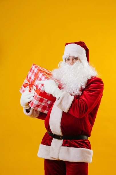 Santa points a finger to something on the right, he holding a big gift - Foto, Imagen
