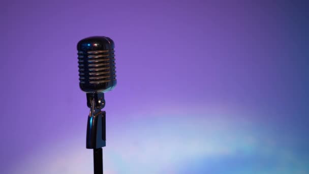 Professionelle Konzert Vintage Blendung Mikrofon für Platte oder sprechen Sie mit dem Publikum auf der Bühne in dunklen leeren Retro-Club in Großaufnahme. Scheinwerfer leuchten auf einem Chrommikrofon links auf blauviolettem Hintergrund.  - Filmmaterial, Video