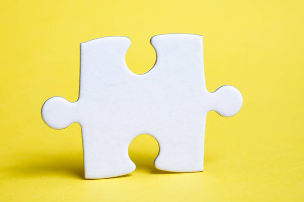 A piece of white puzzle on a yellow background. The concept of the necessary details for the task. - Photo, Image