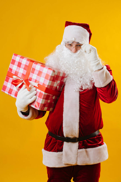 Santa looking at the camera and adjusting glasses, he holding a big gift  - Foto, Imagen