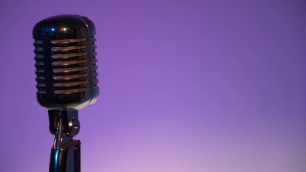Metallic concert vintage glare microphone for record or speak to audience on stage in dark άδειο ρετρό club close up. Προβολείς λάμπουν σε ένα μικρόφωνο χρωμίου στα αριστερά σε μωβ φόντο χρώμα.  - Πλάνα, βίντεο