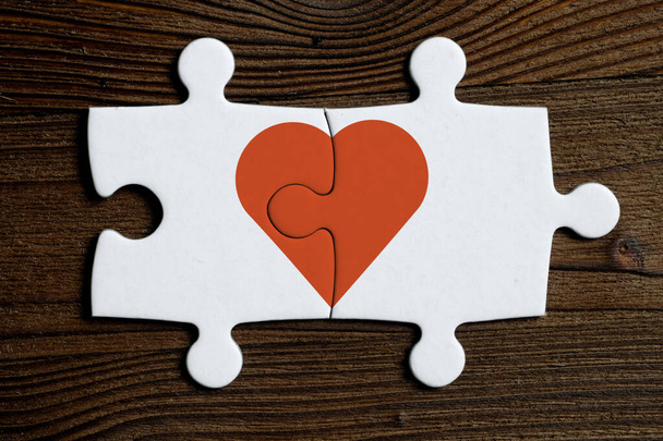 Het concept van wederzijdse liefde. Stukken van een aaneengesloten witte puzzel met rood hart op een houten achtergrond. - Foto, afbeelding