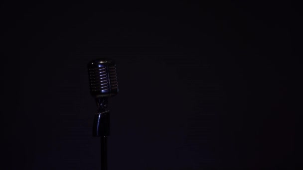 Egy gyönyörű fénypontja a reflektorfényből mozog a professzionális koncert vintage vakító mikrofon rögzíteni vagy beszélni közönség a színpadon sötét üres retro klub fekete alapon. - Felvétel, videó