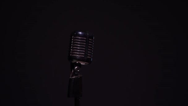 Professzionális koncert vintage vakító mikrofon rögzítésére vagy beszélni közönség a színpadon sötét üres térben közeli. Piros, fehér és zöld reflektorok ragyognak króm retro mikrofon fekete alapon. - Felvétel, videó