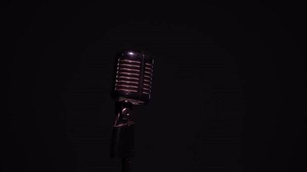 Metallic concert vintage verblindende microfoon voor opname of spreken tot publiek op het podium in donkere lege club close-up. Rode, witte en groene spots verlichten een chromen retro microfoon op zwarte achtergrond. - Video