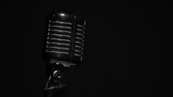 Professionele concert vintage glare microfoon voor opname of spreken met publiek op het podium in donkere lege ruimte close-up. Witte spots schijnen op een chromen retro microfoon aan de linkerkant op zwarte achtergrond. - Video