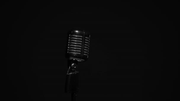 Professionele concert vintage glare microfoon voor opname of spreken met publiek op het podium in donkere lege ruimte close-up. Witte spots schitteren op een chromen retro microfoon in het midden op zwarte achtergrond. - Video