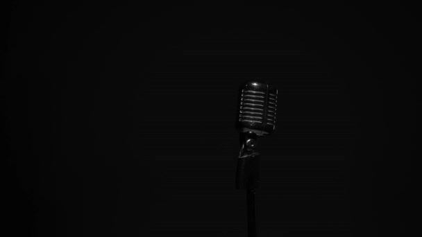 Professionele concert vintage glare microfoon voor opname of spreken met publiek op het podium in donkere lege ruimte close-up. Witte schijnwerpers schijnen op een chromen retro microfoon aan de rechterkant op zwarte achtergrond. - Video