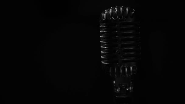 Glans van wit licht flikkert en schijnt op een chromen retro microfoon op zwarte achtergrond. Professionele vintage glare microfoon voor opname of spreken met publiek op het podium in donkere lege ruimte close-up. - Video