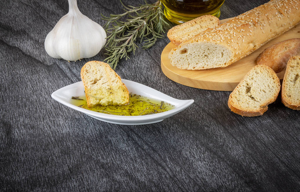 Baguette und Olivenöl-Dip. köstliche griechische Snacks und Getränke. Olivenöl mit Kräutern und Knoblauch. Brot-Olivenöl-Sauce auf Holzgrund.  - Foto, Bild