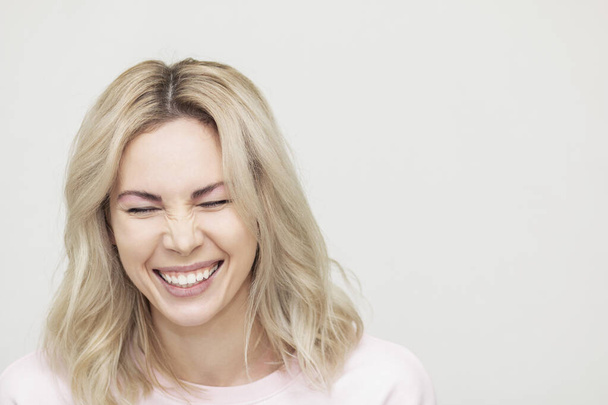 красивая девушка, смеющаяся перед камерой, играющая и веселая, красивая блондинка на розовом фоне
 - Фото, изображение