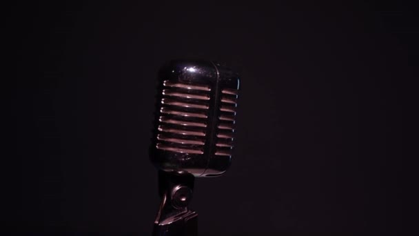 Professionele vintage glare microfoon voor opname of spreken met publiek op het podium in donkere lege club close-up. Witte spots schitteren op een chromen retro microfoon op zwarte achtergrond. Camera draait om. - Video