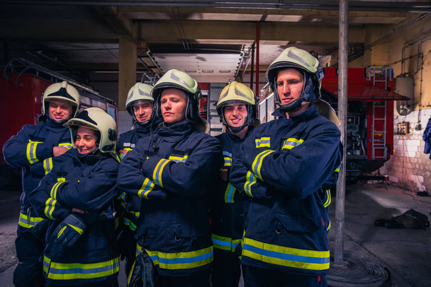 Retrato de bomberos de grupo frente al camión de bomberos dentro de la estación de bomberos
 - Foto, imagen