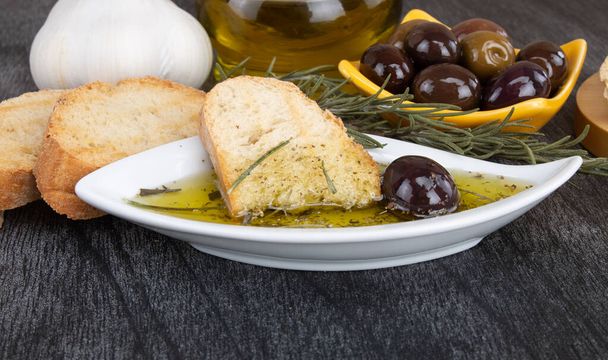 Chleb zanurzony w oliwie z oliwek. Grecka oliwa z oliwek. Włoski chleb z olejem do zanurzania z ziół i przypraw. Sos oliwy z oliwek w białej misce i greckich oliwek na tle drewna.  - Zdjęcie, obraz