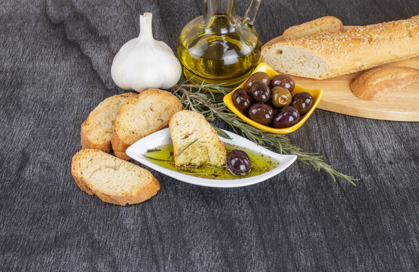 The bread dipped in olive oil with olive. Greek olive oil bread dip. Olive oil sauce in white bowl & Greek olives on wood background. Copy space for text. Bread dipping concept mediterranean food. - Foto, Bild