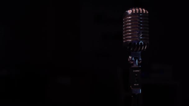 Professionele concert vintage glare microfoon voor opname of spreken met publiek op het podium in donkere lege ruimte close-up. Spotlights schitteren op een chromen retro microfoon aan de rechterkant op zwarte achtergrond. - Video