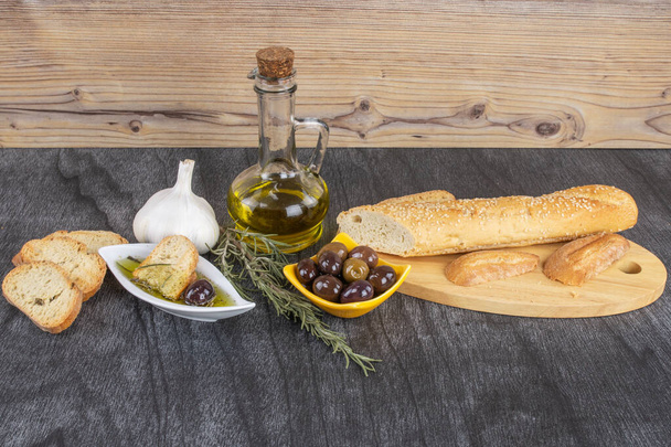 Brotdip, Olivenöl, Knoblaucholiven und Rosmarin auf grauem Holztisch. Kopierraum für Text. natürliche Delikatessen. griechische Olivenölsoße. - Foto, Bild