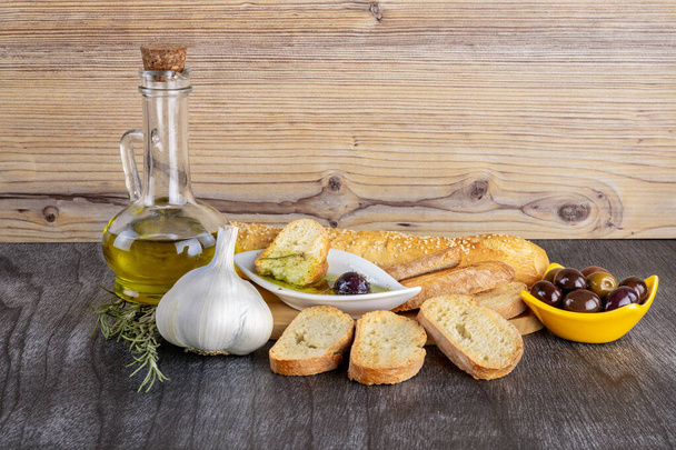 The bread dipped in olive oil with olive. Greek olive oil bread dip. Greek sauce in white bowl & Greek olives on wood background. Olive oil and spices. Bread dipping concept. - 写真・画像