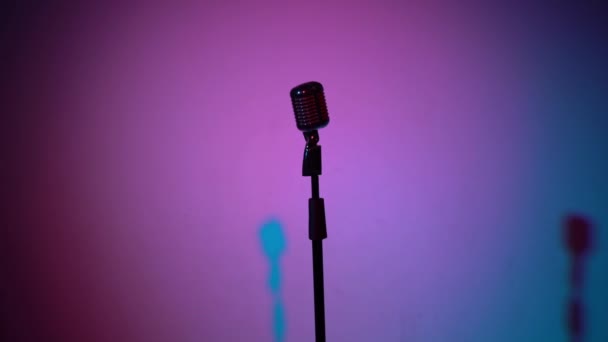 Professionele vintage glare microfoon voor opnemen of spreken op het podium in donkere lege retro club close-up. Spotlights schijnen op een chroom microfoon in het midden op multi color achtergrond. De camera nadert.. - Video