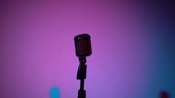 Professzionális ezüst vintage vakító mikrofon rögzítésére, vagy beszéljen a közönség a helyszínen sötét üres retro klub közeli. Spotlights ragyog egy króm mikrofon lila és kék háttér. - Felvétel, videó