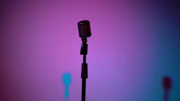 Microphone classique argenté éblouissant pour enregistrer ou parler sur scène dans un club rétro sombre vide de près. Les projecteurs brillent sur un micro chromé au milieu sur fond multicolore. La caméra s'approche.
. - Séquence, vidéo