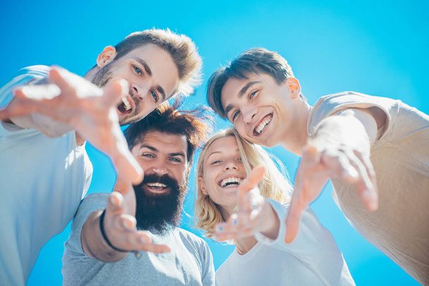Excited people. Group of happy cheerful smiling friends offer their hands down to the camera at clear blue sky background. Summertime and friendship concept. Teammates gather together and have fun. - Photo, Image