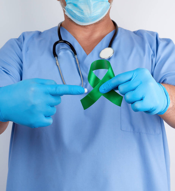 Mavi üniformalı doktor ve lateks eldivenli doktor yeşil bir kurdele tutuyor.  - Fotoğraf, Görsel